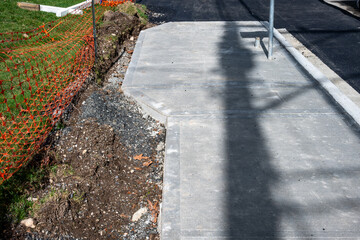 Obraz premium Public works road paving and sidewalk installation project, fresh asphalt and new cement sidewalk with storm drain at curb 