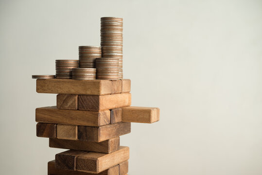 Stack coins on danger wood tower block game with white wall background copy space. Concept of business risk management, global economic crisis, financial bank run or bankruptcy, loss in investment.