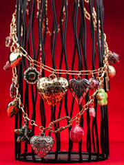 Close up of golden necklaces with pendants with hearts, flowers and beads on red background