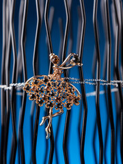 Close up of golden brooch in shape of ballerina dancer with black rhinestones on blue background