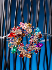 Close up of brooch in the shape of a flower wreath with leaves with multicolored stones and...