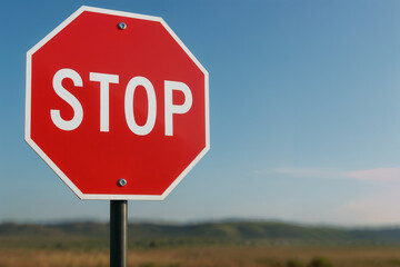 Obraz premium Red Stop Sign On Black Pole Against Blue Sky And Brown Grass Field Background