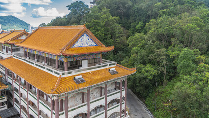 The buildings of the Chinese temple. Orange tiled roofs with curved cornice edges. Ornaments on the walls. Terraces with columns. Green tropical vegetation. Blue sky, clouds. Malaysia. Penang.   © Вера 