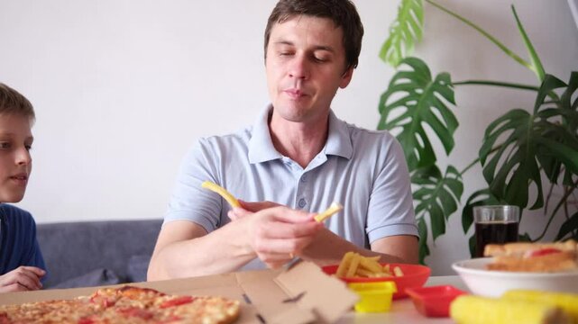 Caucasian kid boy and his father eating junk food at home. Single Father and son fast food, unhealthy food concept. Part of series
