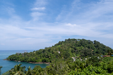 Lush tropical coastline of Gunuang Padang, Padang, West Sumatra, Indonesia, featuring a mix of vibrant green foliage and bare trees overlooking the calm blue ocean
