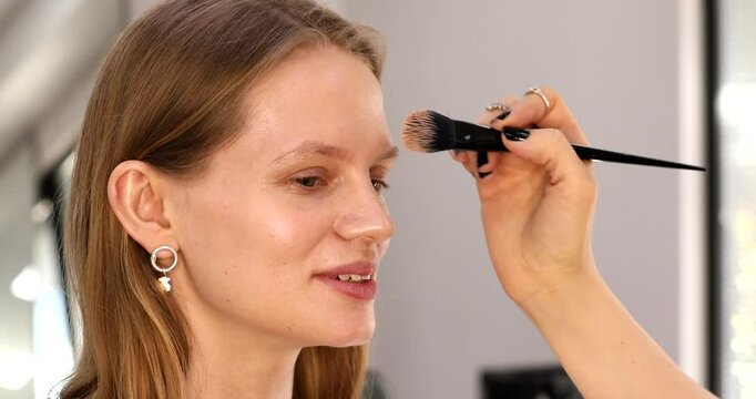 Professional makeup artist working with beautiful young woman. Makeup artist applying makeup on glamour model 