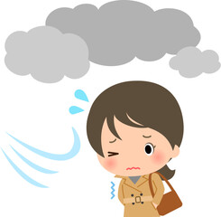 曇天の下を寒そうに歩くトレンチコートの女性