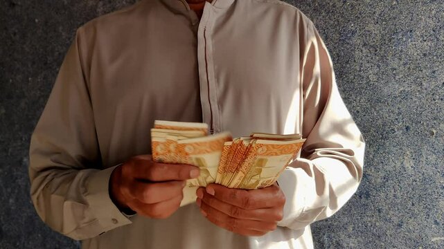 A man counting 5000 Pakistani rupee notes financial management and currency concept
