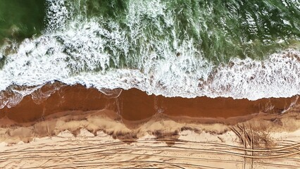 Aerial View of Waves Crashing on the Namibian Coastline with Car Tracks on the Sand