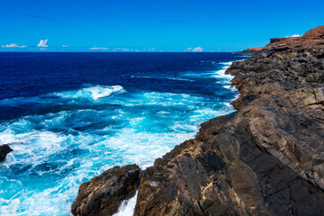 Obraz premium Stunning Coastal Landscape of Fuerteventura with Turquoise Waves Breaking Against Dark Volcanic Cliffs. Dramatic Ocean Scenery from Canary Islands