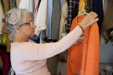 Senior woman choosing orange jacket from wardrobe closet