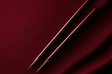 Naklejka premium Two elegant pencils on a rich red fabric background, creating a minimalist design.