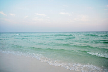 Obraz premium Gentle turquoise waves rolling onto a sandy beach under a pastel sky