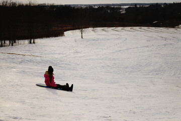 Side view young girl riding sled down snowy hill