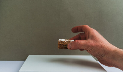 Hand holding a small piece of dessert with a textured surface in a minimalistic setting
