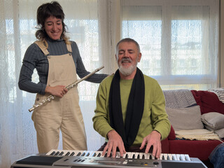 A man and a woman are playing a keyboard together. The woman is holding a flute. Scene is happy and friendly