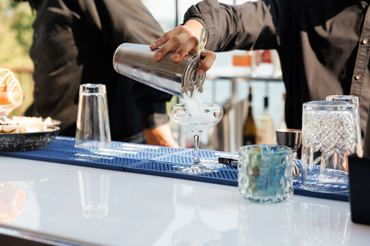 Male bartender pours a cocktail in a summer bar. Close-up of a bartender's hand pouring a drink from a silver shaker into a glass. A bartender makes a cool summer cocktail at the hotel bar outside