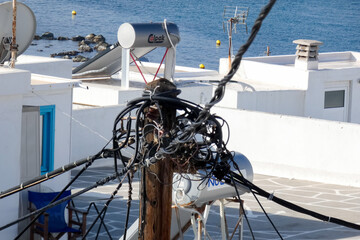 Messy electrical wires tangled on wooden pole on building rooftop by sea