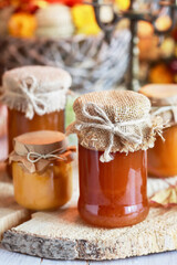 Jars of honey on a wooden stand, surrounded by autumn flowers.