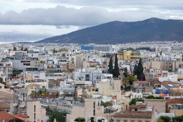 Athens cityscape expanding towards mountains under cloudy sky