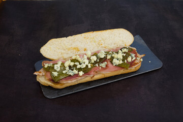 A sandwich with ham, cheese, and green peppers on a black plate