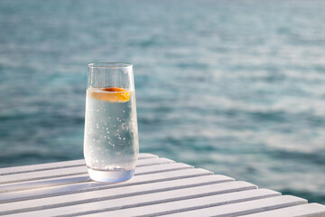 Chilled glass of water with slice of orange on a white table