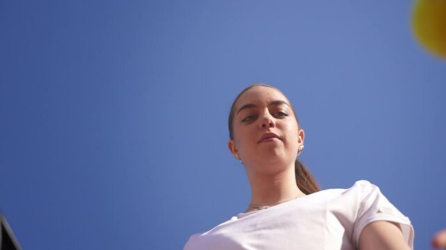 Suggestive low-angle shot of a beautiful teenage girl tennis player bouncing the ball to serve on a clay court.