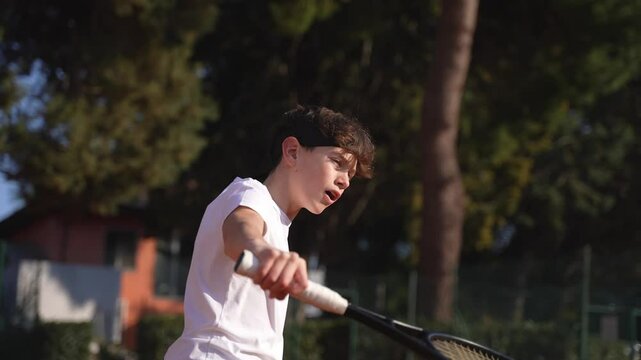 Slow motion, suggestive frontal shot of a handsome teenage boy playing tennis in summer, vol&egrave;e at net.