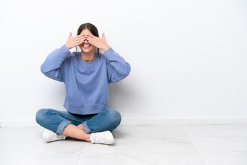 Young caucasian woman sitting on the floor isolated on white background covering eyes by hands