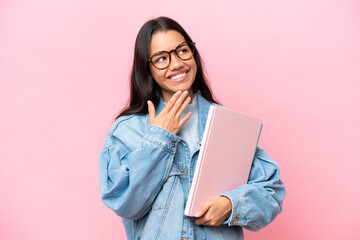 Fototapeta premium Young student Colombian woman isolated on pink background looking up while smiling