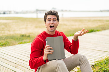 Fototapeta premium Young handsome man holding a tablet at outdoors with shocked facial expression