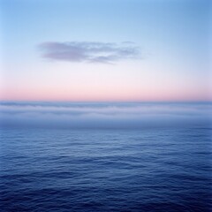 Obraz premium A cloud-like mist rising above a calm ocean at dawn