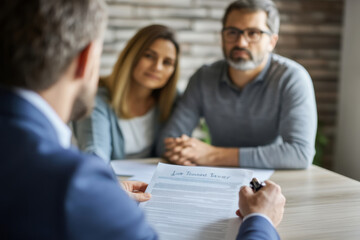 In an office setting, a lawyer clarifies a legal document to a couple, providing guidance and answering questions. The atmosphere is focused and professional, emphasizing clear communication