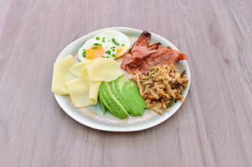 A plate of food with a piece of bacon, an egg, and avocado