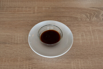 A small white bowl of sauce sits on a wooden table