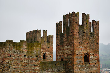 ancient brick fortress with towering battlements, a medieval stronghold standing against time, surrounded by misty hills and historic charm