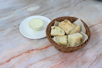 A basket of bread and a white plate with a yellow dip