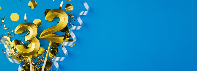 Celebrating 32 years. Golden burning candle in form of number thirty two on celebration festive blue background lying in sparkles. Holiday banner with copy space.