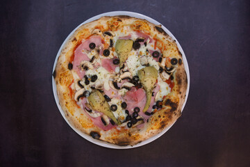 A pizza with mushrooms, olives, and ham on a white plate