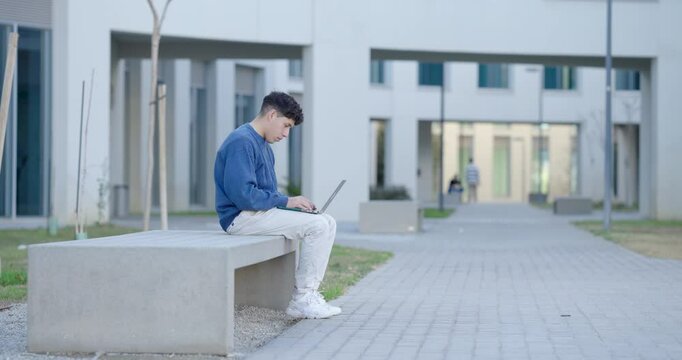 Student working on laptop outside university building
