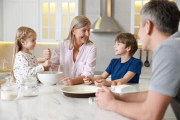 Little kids with their father and grandmother making dough at marble table in kitchen