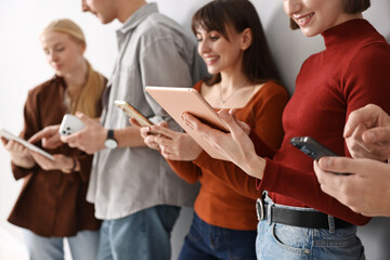 Group of people using different gadgets near light wall indoors. Modern technology