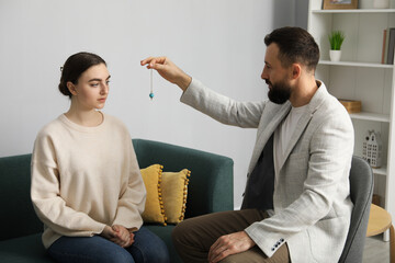 Psychologist using pendulum while working with patient during hypnosis session indoors