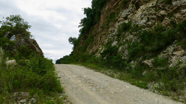 Dirt road in rocky mountains. Dirt road runs along the mountainside of a tropical island, among stones and rocks. - Powered by Adobe