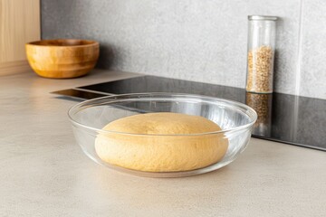 Freshly kneaded dough rising in a glass bowl on a modern kitchen countertop with grains