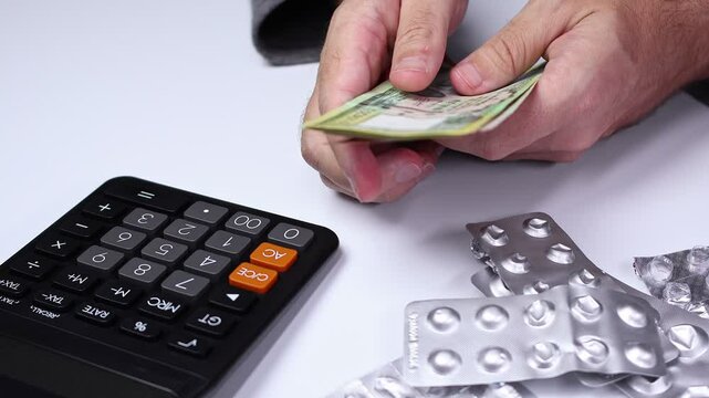 Macro shot of calculator, used empty pill blisters and man's hands counting Nepalese rupee (NPR) banknotes. Medicine healthcare in Nepal. Concept of buying drugs, medication, vitamins. Close up view.