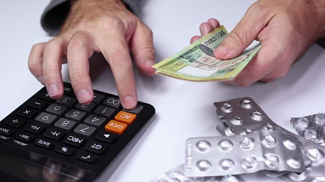 Macro shot of calculator, used empty pill blisters and man's hands counting Nepalese rupee (NPR) banknotes. Medicine healthcare in Nepal. Concept of buying drugs, medication, vitamins. Close up view.