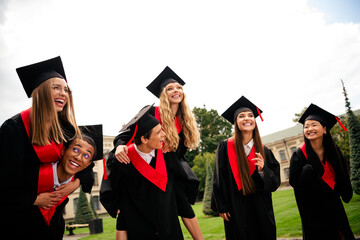 Joyful group of graduating students celebrating their achievement in cap and gown outdoors on a...