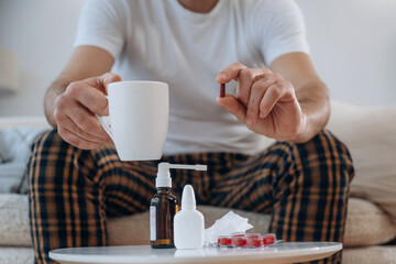 Table with cup and spray. Guy is sitting and taking a pills, feeling sick, bad