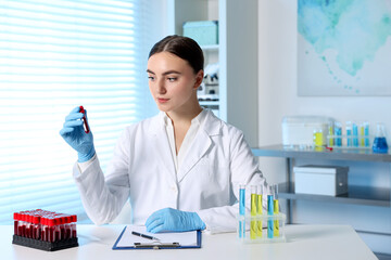 Laboratory testing. Doctor holding test tube with blood sample at table indoors